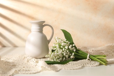 Photo of Beautiful lilies of the valley flowers and vase on white table near beige wall