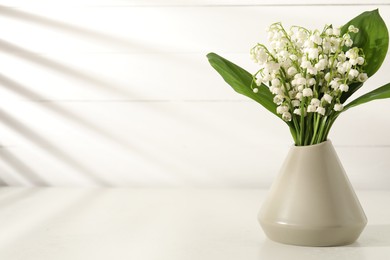 Photo of Beautiful lilies of the valley flowers in vase on white table. Space for text