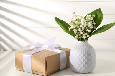 Photo of Beautiful lilies of the valley flowers and gift on white table. Space for text