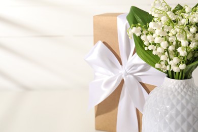 Photo of Beautiful lilies of the valley flowers and gift on white table, closeup. Space for text