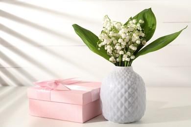 Photo of Beautiful lilies of the valley flowers and gift on white table