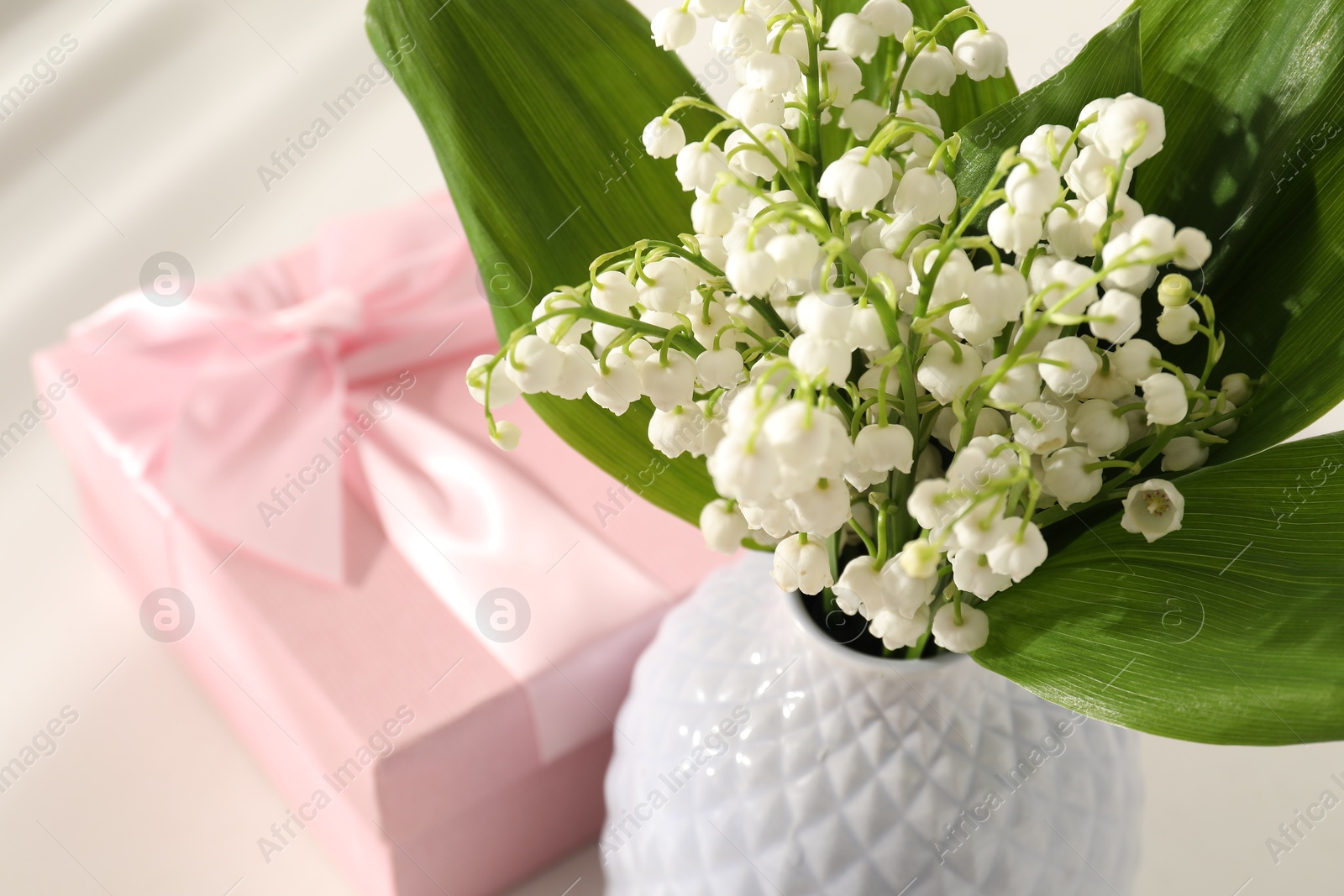 Beautiful lilies of the valley flowers and gift on white table, closeup Photo of Beautiful lilies of the valley flowers and gift on white table, closeup