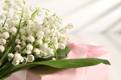 Photo of Beautiful lilies of the valley flowers and gift on white table, closeup. Space for text