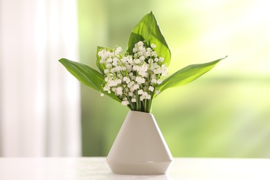 Photo of Beautiful lilies of the valley flowers in vase on white table against blurred background