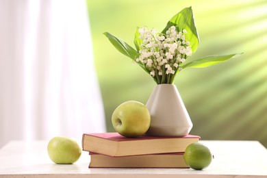 Photo of Beautiful lilies of the valley flowers in vase, fruits and books on white table against blurred background. Space for text
