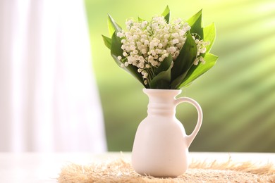 Photo of Beautiful lilies of the valley flowers in vase on white table against blurred background. Space for text