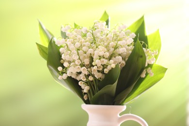 Photo of Beautiful lilies of the valley flowers in vase against blurred background, closeup