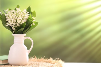 Photo of Beautiful lilies of the valley flowers in vase and book on white table against blurred background. Space for text