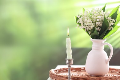 Photo of Beautiful lilies of the valley flowers in vase and candle on white table against blurred background. Space for text