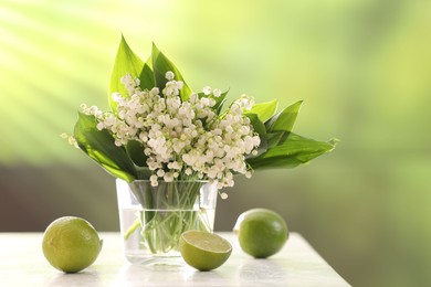 Photo of Beautiful lilies of the valley flowers in vase and limes on white table against blurred background