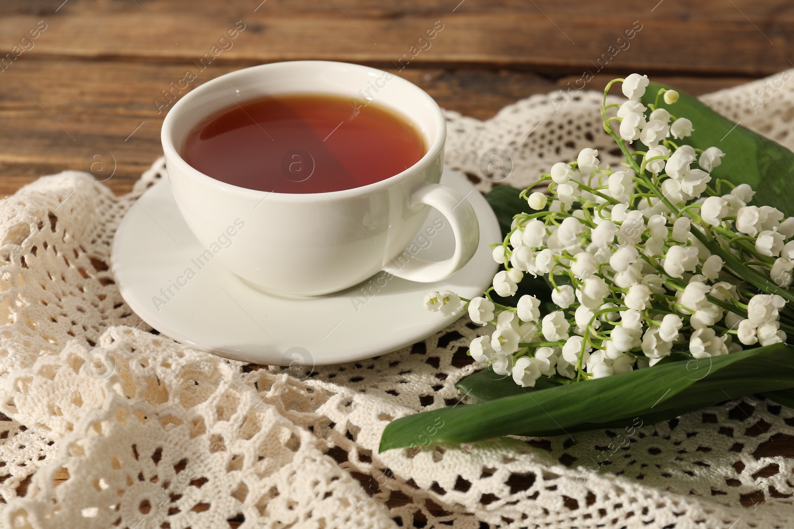 Beautiful lilies of the valley flowers and tea on wooden table, closeup Photo of Beautiful lilies of the valley flowers and tea on wooden table, closeup