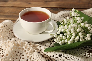 Photo of Beautiful lilies of the valley flowers and tea on wooden table, closeup