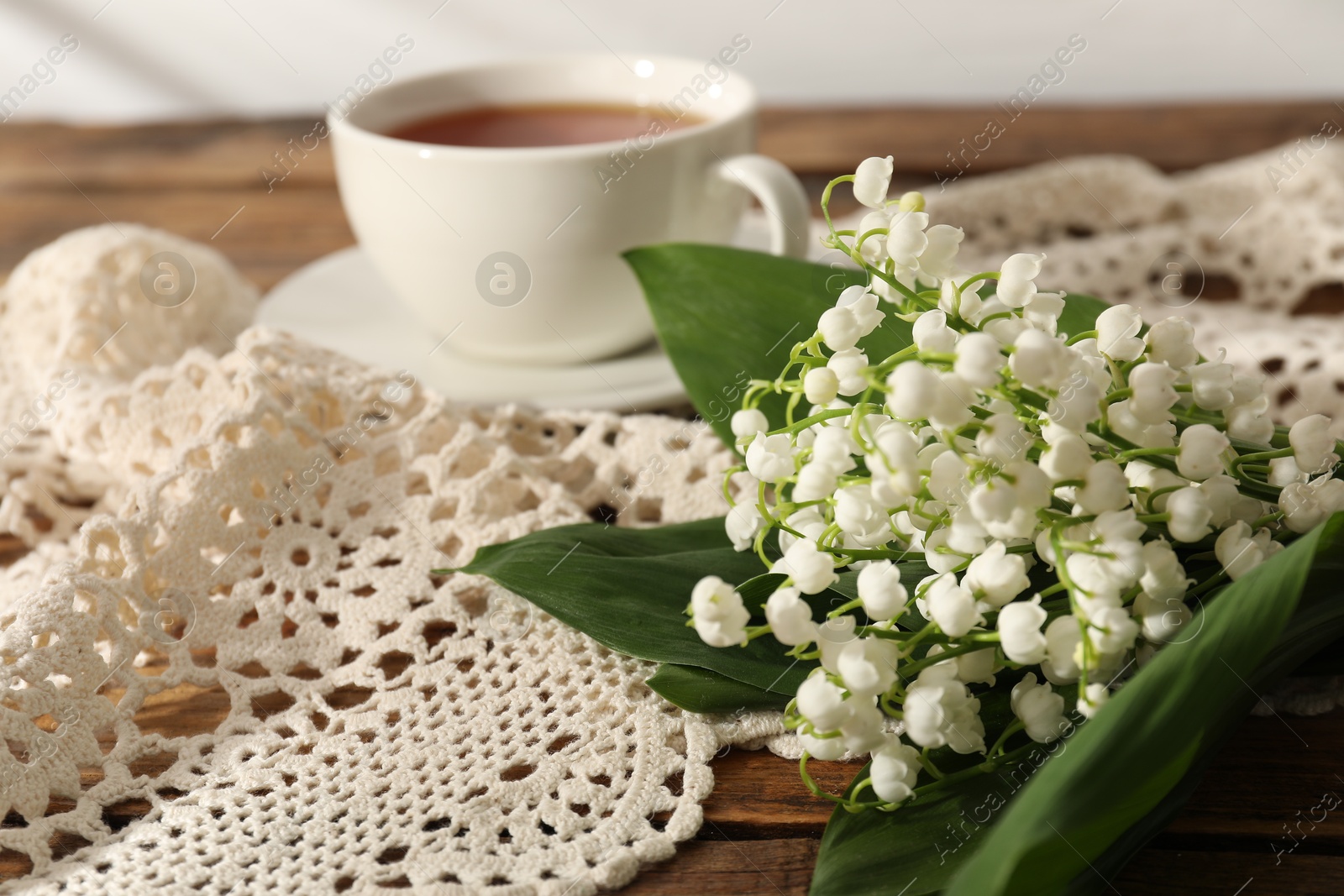 Beautiful lilies of the valley flowers and tea on wooden table, closeup Photo of Beautiful lilies of the valley flowers and tea on wooden table, closeup
