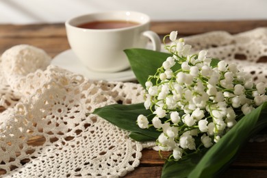 Photo of Beautiful lilies of the valley flowers and tea on wooden table, closeup