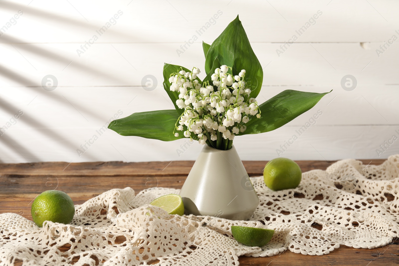 Beautiful lilies of the valley flowers in vase and limes on wooden table Photo of Beautiful lilies of the valley flowers in vase and limes on wooden table