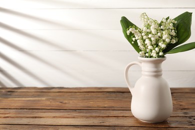 Photo of Beautiful lilies of the valley flowers in vase on wooden table. Space for text