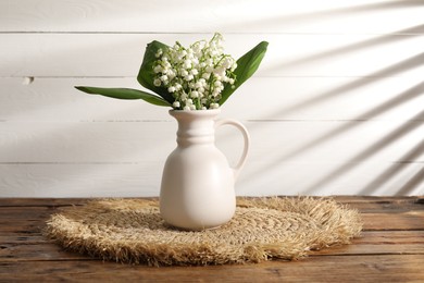 Photo of Beautiful lilies of the valley flowers in vase on wooden table