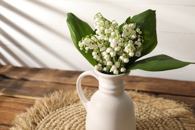 Photo of Beautiful lilies of the valley flowers in vase on wooden table, closeup