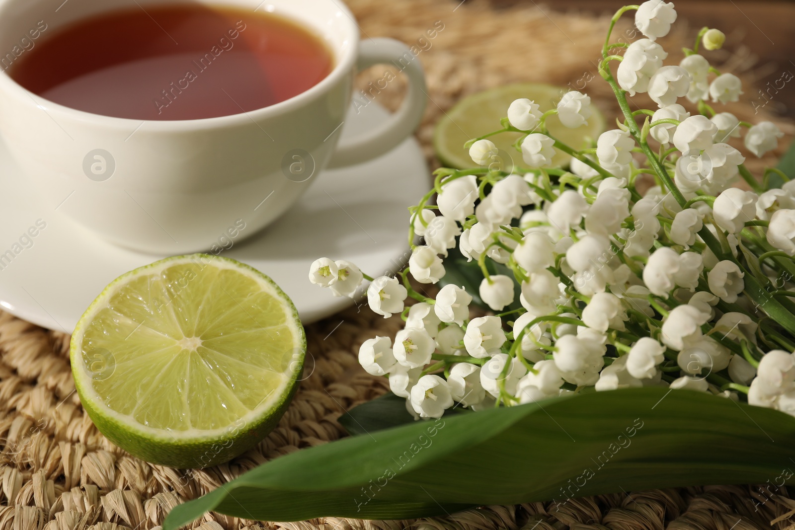 Beautiful lilies of the valley flowers, tea and limes on table, closeup Photo of Beautiful lilies of the valley flowers, tea and limes on table, closeup