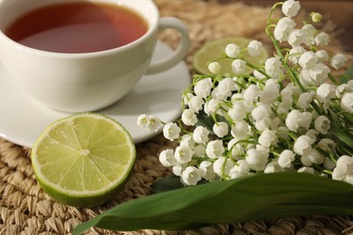 Photo of Beautiful lilies of the valley flowers, tea and limes on table, closeup