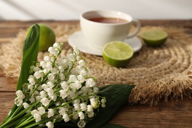 Photo of Beautiful lilies of the valley flowers, tea and limes on wooden table, closeup