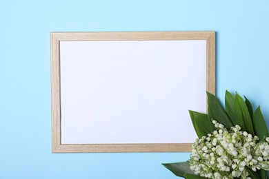 Photo of Beautiful lily-of-the-valley flowers and blank frame on light blue background, top view. Space for text