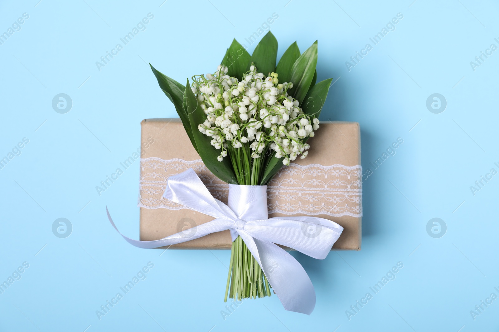 Beautiful lily-of-the-valley flowers and gift on light blue background, top view Photo of Beautiful lily-of-the-valley flowers and gift on light blue background, top view