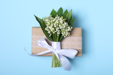 Photo of Beautiful lily-of-the-valley flowers and gift on light blue background, top view