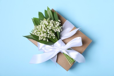 Photo of Beautiful lily-of-the-valley flowers and gift on light blue background, top view