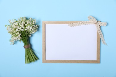 Photo of Beautiful lily-of-the-valley flowers and blank frame on light blue background, top view. Space for text