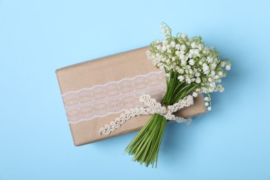 Photo of Beautiful lily-of-the-valley flowers and gift on light blue background, top view