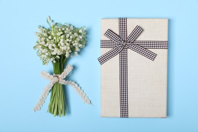 Photo of Beautiful lily-of-the-valley flowers and gift on light blue background, top view