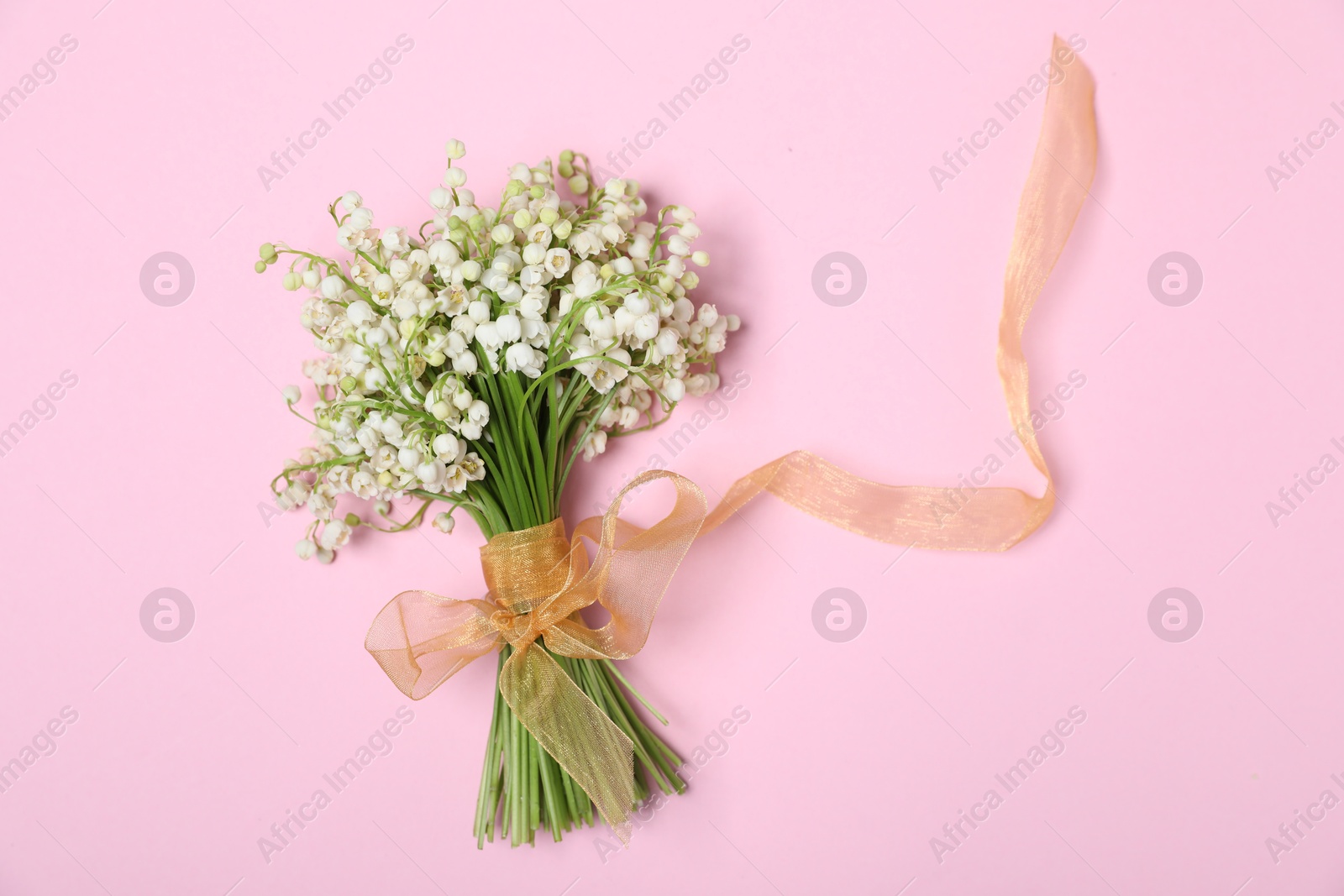 Beautiful lily-of-the-valley flowers on light pink background, top view Photo of Beautiful lily-of-the-valley flowers on light pink background, top view