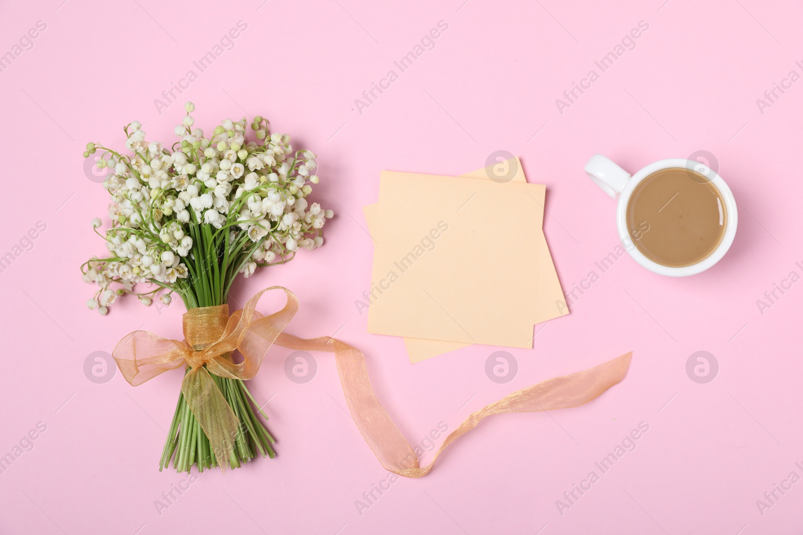 Beautiful lily-of-the-valley flowers, notes and coffee on light pink background, flat lay Photo of Beautiful lily-of-the-valley flowers, notes and coffee on light pink background, flat lay
