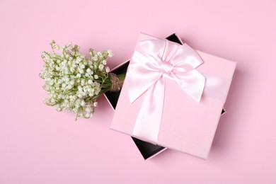 Photo of Beautiful lily-of-the-valley flowers and gift on light pink background, top view