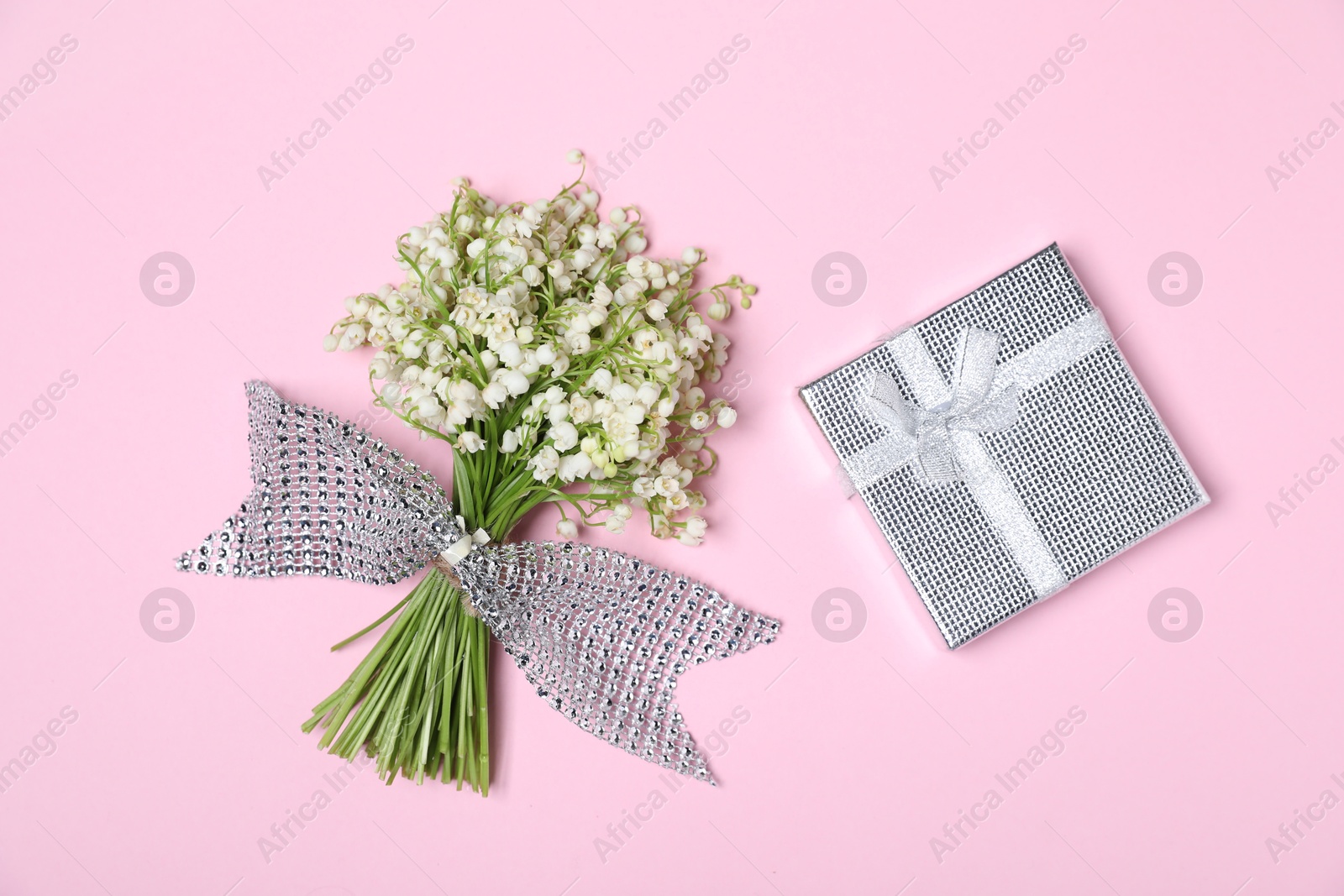 Beautiful lily-of-the-valley flowers and gift on light pink background, top view Photo of Beautiful lily-of-the-valley flowers and gift on light pink background, top view
