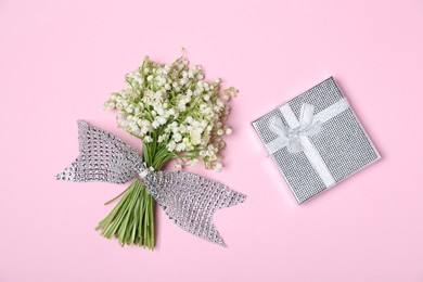 Photo of Beautiful lily-of-the-valley flowers and gift on light pink background, top view