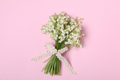 Photo of Beautiful lily-of-the-valley flowers on light pink background, top view