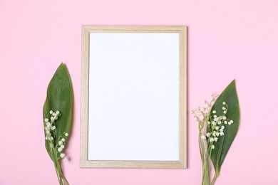 Photo of Beautiful lily-of-the-valley flowers and blank frame on light pink background, flat lay. Space for text
