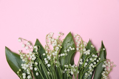 Photo of Beautiful lily-of-the-valley flowers and leaves on light pink background, flat lay. Space for text
