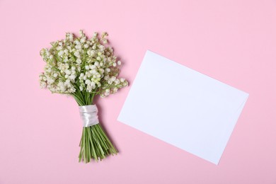 Photo of Beautiful lily-of-the-valley flowers and envelope on light pink background, top view