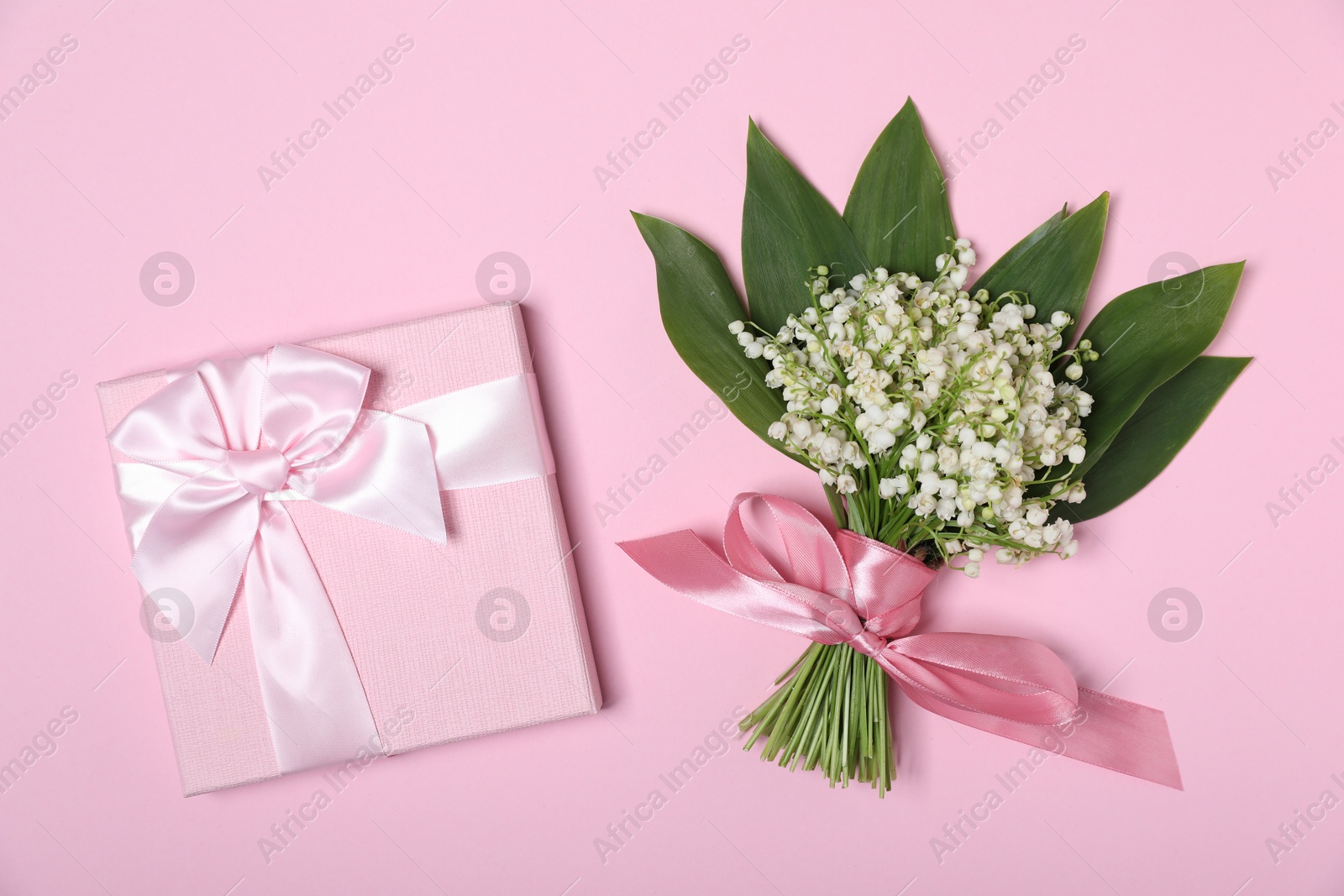 Beautiful lily-of-the-valley flowers and gift on light pink background, top view Photo of Beautiful lily-of-the-valley flowers and gift on light pink background, top view