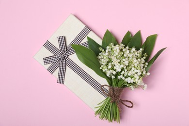 Photo of Beautiful lily-of-the-valley flowers and gift on light pink background, top view