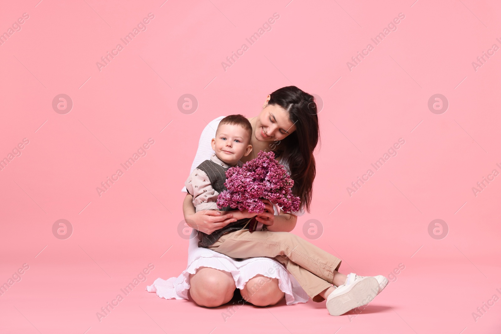 Mother and her son with bouquet of lilac flowers on pink background Photo of Mother and her son with bouquet of lilac flowers on pink background