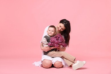 Photo of Mother and her son with bouquet of lilac flowers on pink background