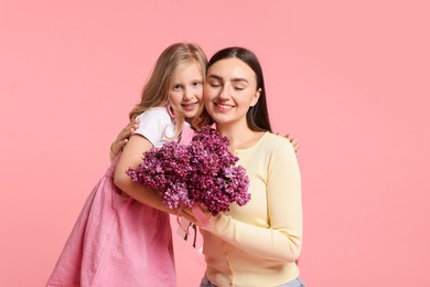 Photo of Mother and her daughter with bouquet of lilac flowers on pink background, space for text