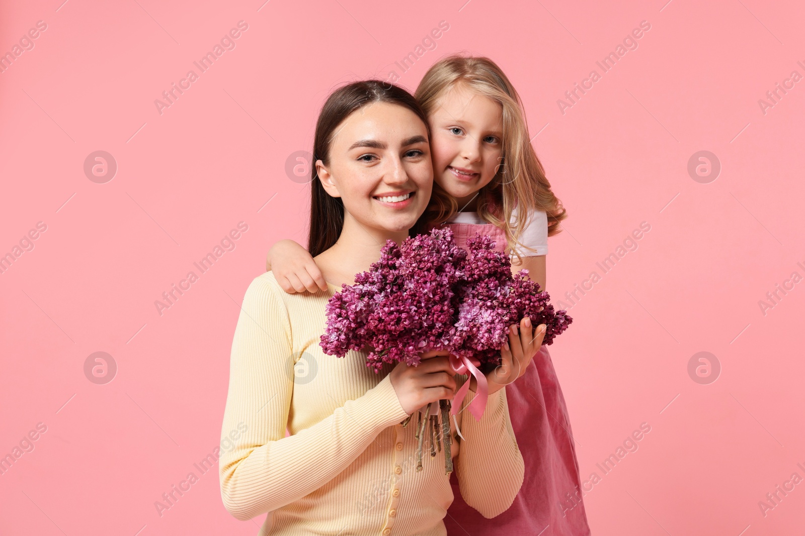 Mother and her daughter with bouquet of lilac flowers on pink background Photo of Mother and her daughter with bouquet of lilac flowers on pink background