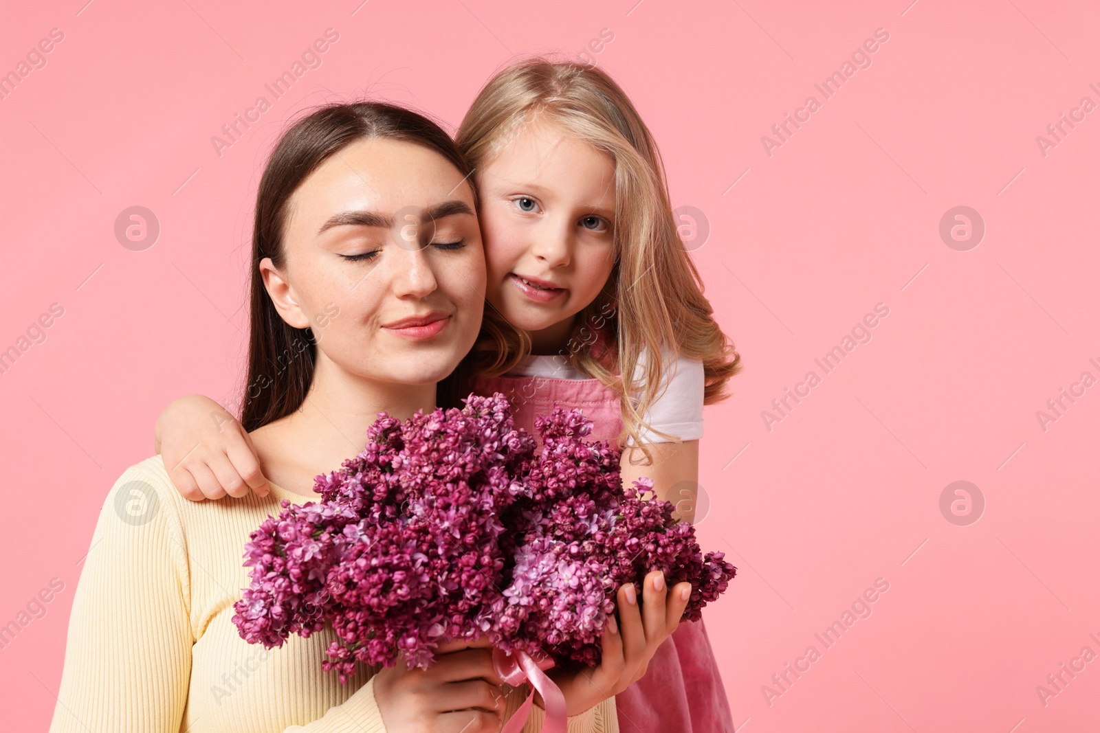 Mother and her daughter with bouquet of lilac flowers on pink background, space for text Photo of Mother and her daughter with bouquet of lilac flowers on pink background, space for text