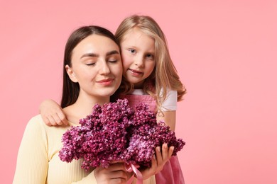 Photo of Mother and her daughter with bouquet of lilac flowers on pink background, space for text
