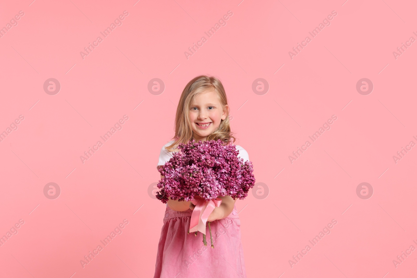 Little girl with bouquet of lilac flowers on pink background Photo of Little girl with bouquet of lilac flowers on pink background